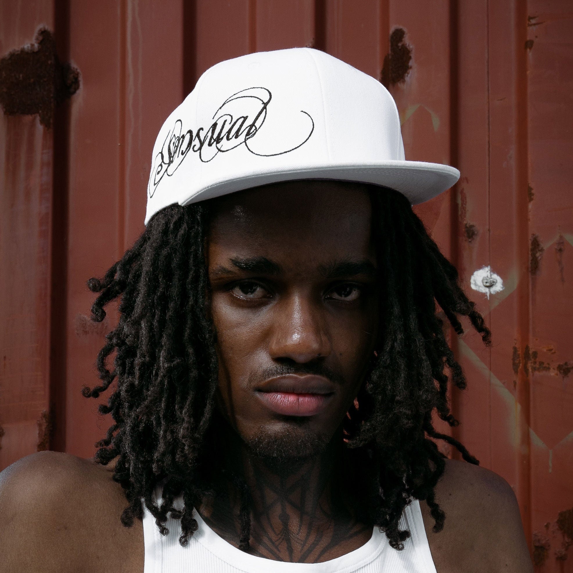 Person wearing a white cap and tank top against a red background